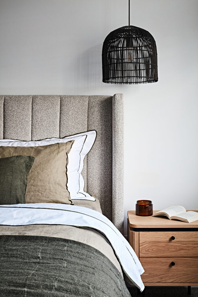Layered main bedroom featuring upholstered bedhead, timber bedside table, linen bedding and black pendant light in a Hampton East home styled by Lisa Hunter Interiors.