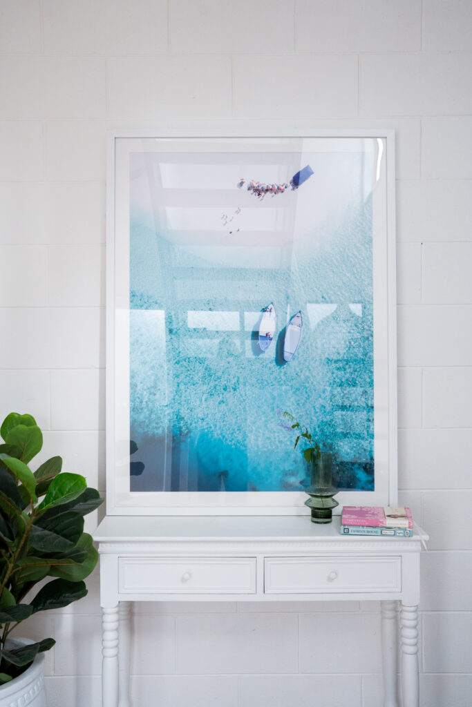 Framed coastal photography styled on a white console with plant styling and decorative accessories in a modern Australian interior.