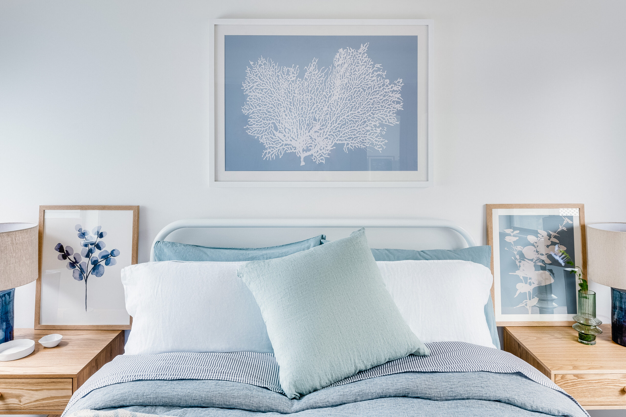 Calm modern coastal bedroom styled with layered blue textiles, oak bedside tables and curated artwork by a Melbourne interior designer