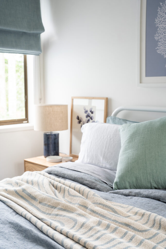 Close-up of layered bedroom textiles with blue cushions, patterned throw and timber bedside styling in a modern coastal home.