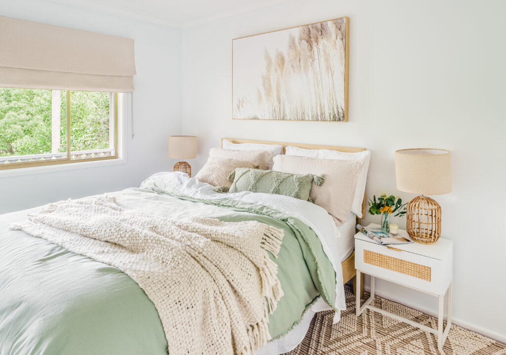 Modern organic bedroom styled with layered green bedding, natural timber furniture, woven textures and soft window furnishings in Melbourne.