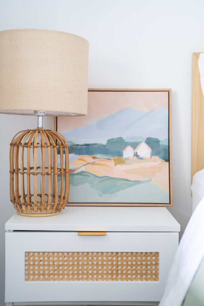 Bedside styling with woven cane lamp, framed artwork and timber bedside table in a modern organic bedroom in Melbourne.