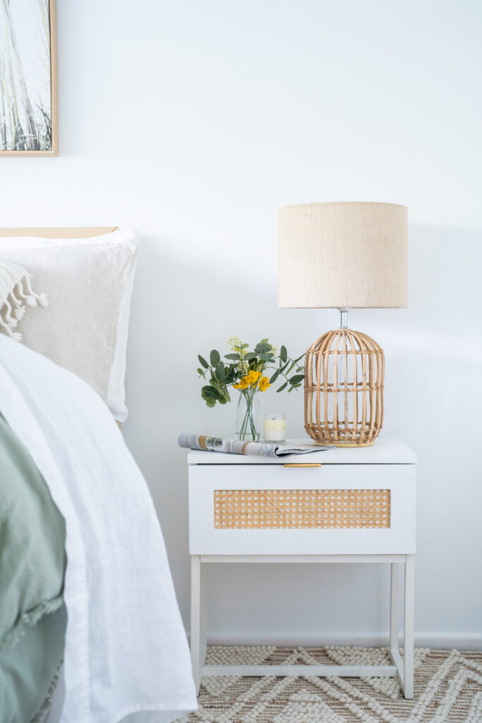 Bedside styling featuring cane table lamp, natural timber bedside table and layered bedding in a modern organic bedroom in Melbourne.