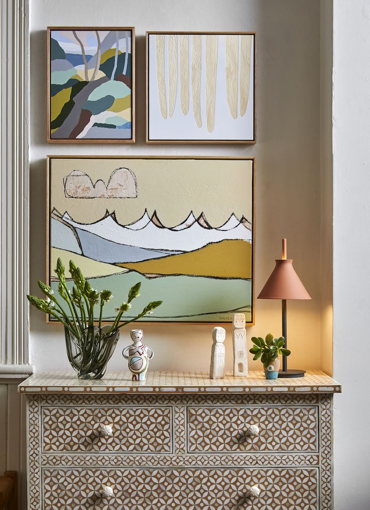 Small gallery wall arrangement above a patterned chest of drawers featuring layered framed artwork and decorative styling in a curated interior.