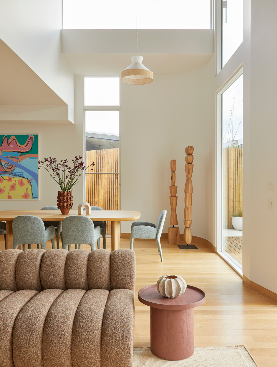 Light filled modern Australian dining and living room featuring sculptural furniture, soft neutral tones, natural timber and double height ceilings.