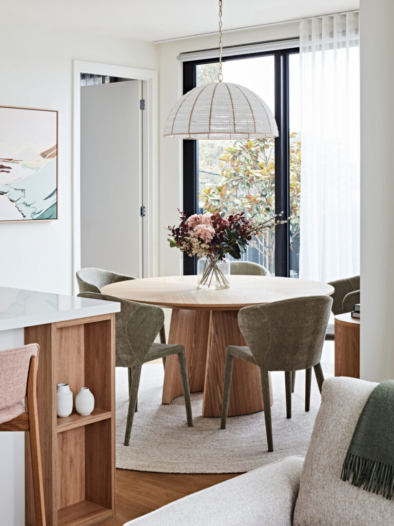 Hampton apartment dining room designed by Lisa Hunter Interiors, featuring a round timber dining table, olive green upholstered chairs, beaded pendant light and sheer curtains.
